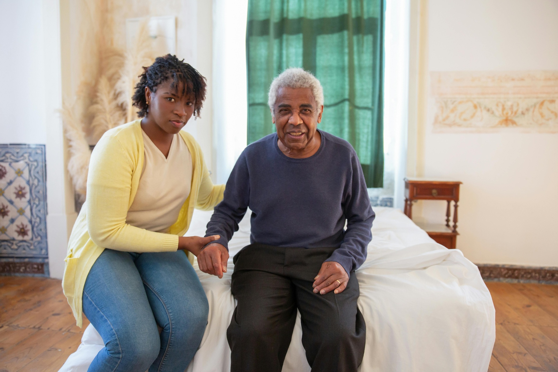 Caregiver sitting with an elderly African man on a bed